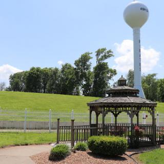 A serene outdoor scene featuring a gazebo and a water tower against a backdrop of green hills.