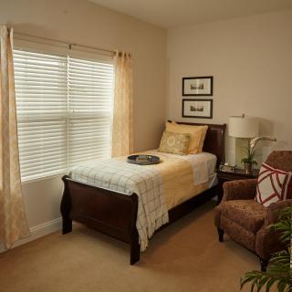 A cozy bedroom with a single bed, armchair, and window with curtains.