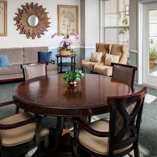 A cozy living room with a round wooden table surrounded by chairs, a comfortable sofa with decorative pillows, and wall adornments including art and a mirror.
