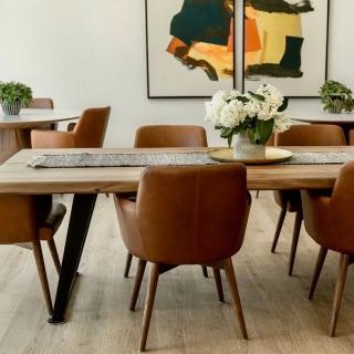 A modern dining room with leather chairs, a wooden table adorned with flowers, and abstract artwork on the wall.
