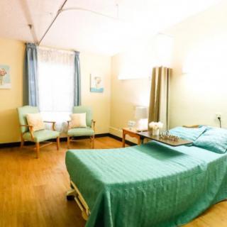 A brightly lit hospital room with two patient beds, chairs, and curtains.