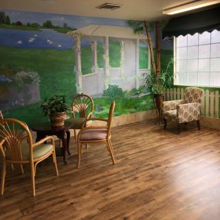 A cozy room with a mural on the wall, featuring a table and chairs, with natural light coming through a window.