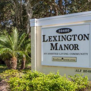 A sign for Lexington Manor, an assisted living community, surrounded by greenery and trees.