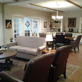 A cozy and elegant living room with a connected dining area, featuring comfortable sofas, armchairs, and a chandelier.