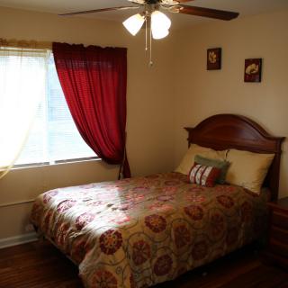 A cozy bedroom with a bed under a window and red curtains.