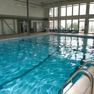 An empty indoor swimming pool with clear water and large windows.