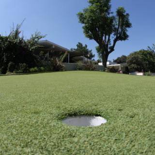A close-up view of a hole on a golf putting green under a clear blue sky.