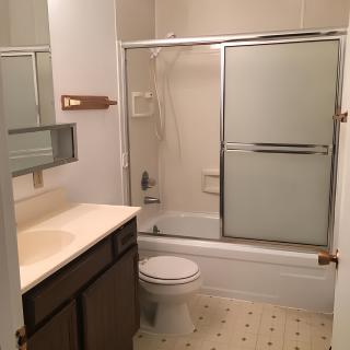 A small bathroom featuring a vanity with a sink and mirror, a toilet, and a bathtub with sliding glass shower doors.