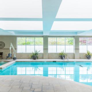A modern indoor swimming pool with large windows and potted plants lining the perimeter.