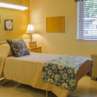 A cozy bedroom featuring a neatly made bed, a soft lamp, and warm yellow walls.