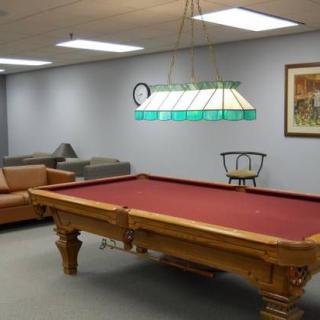 A cozy game room featuring a pool table with red felt, surrounded by sofas and chairs, under a decorative light fixture.