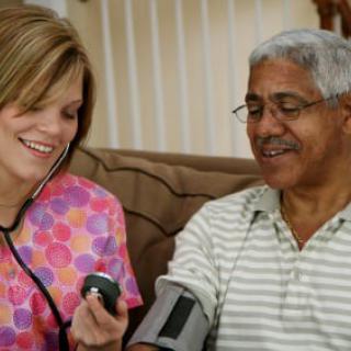 A healthcare professional checks a patient's blood pressure while they both smile.