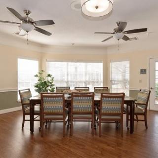 Spacious dining room with a large table and chairs, featuring ceiling fans and ample natural light from surrounding windows.