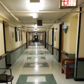 A long, empty hospital corridor with overhead lighting and checkered tile flooring.