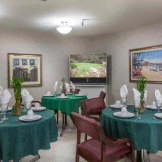 A neatly arranged dining room with green tablecloths and white napkins set on tables, surrounded by chairs and decorated with artwork on the walls.