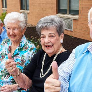 A cheerful group of seniors giving a thumbs up outdoors.