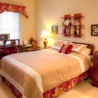 A cozy bedroom with warm lighting, featuring a neatly made bed, decorative shelves, and classic wooden furniture.