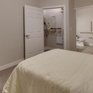 A cozy bedroom with an open closet door and a neatly made bed.