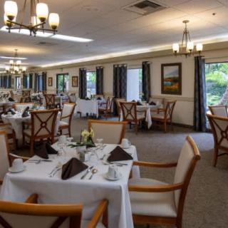 An elegant restaurant dining room with neatly arranged tables and chairs, set with white tablecloths and decorative place settings.