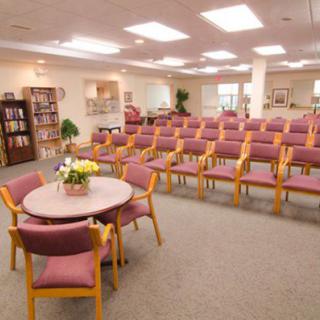 A spacious meeting room with rows of chairs and a small round table, surrounded by bookshelves and soft lighting.