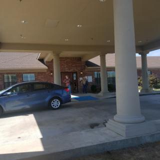 A view of a building entrance with a parked car and columns in the foreground.