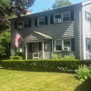 A charming two-story home featuring an American flag and a well-maintained garden.