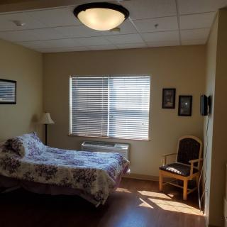 A cozy bedroom with a bed, chair, and window allowing natural light.