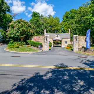 A scenic entrance to a building surrounded by lush greenery and under a partly cloudy sky.