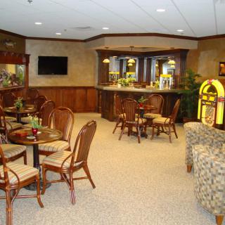 A cozy lounge area featuring a bar, seating with tables and chairs, and a jukebox.