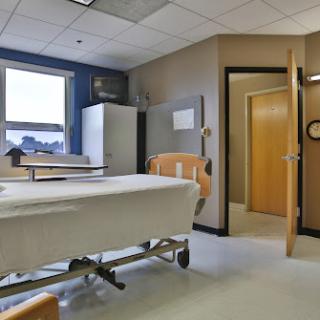 A view of a hospital patient room, featuring a bed, window, and an entrance.