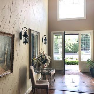 A well-lit foyer with elegant decor, featuring a painting and inviting entry doors.