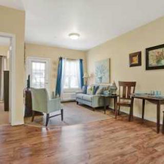A cozy living room with wood flooring, featuring a sofa, armchairs, and wall art.