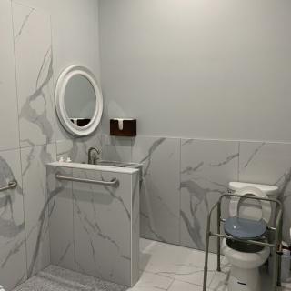 An accessible bathroom with a sink, mirror, toilet, and grab bars, featuring marble tile walls.