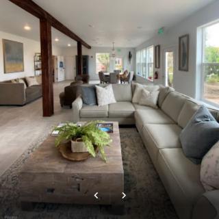 A spacious and well-lit living room featuring a large sectional sofa and a wooden coffee table, with an open floor plan leading to other areas of the home.