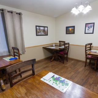 A cozy dining area with wooden tables and chairs, decorated with framed pictures on the walls and a soft curtain on the window.