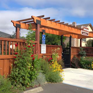 A wooden pergola entrance surrounded by a garden with colorful flowers and a fence.