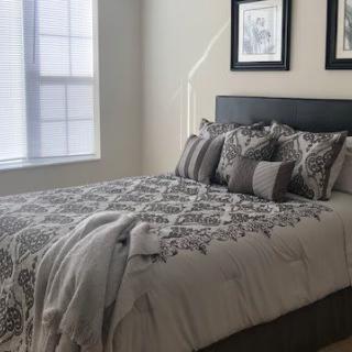 A neatly arranged bedroom with a patterned bedspread, several pillows, and framed artwork on the wall.