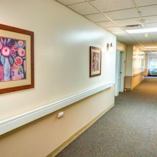 A hospital hallway with artwork adorning the walls and ceiling lights illuminating the corridor.