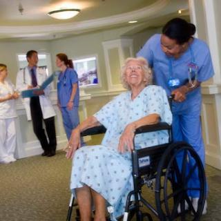 A joyful elderly patient in a wheelchair is surrounded by attentive healthcare professionals in a hospital setting.