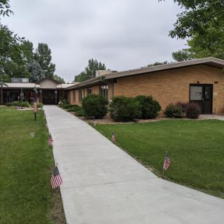 A pathway leading to a single-story brick building surrounded by green lawns and trees.