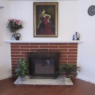 A cozy living room features a brick fireplace adorned with plants, flowers, and artwork.