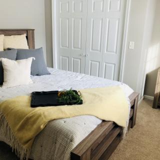 A cozy bedroom with a neatly made bed, featuring a mix of gray and white pillows and a yellow throw blanket, next to a double-door closet.