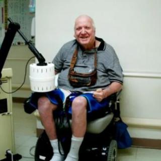 A person sitting in a wheelchair indoors, smiling at the camera.