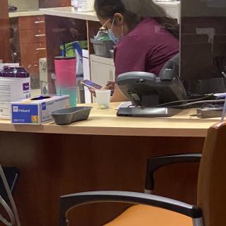 A healthcare worker at a reception desk working on a computer while wearing a mask.