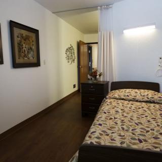 A cozy bedroom with a single bed, decorative paintings on the wall, and wooden flooring.