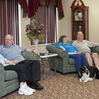 A group of seniors sitting together in a living room with a dog.