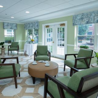 A cozy waiting area with green upholstered chairs and a round coffee table, well-lit by natural light from large windows.