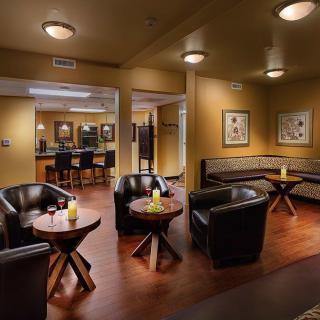 A cozy lounge area with leather chairs and tables, softly lit with wall artwork and wooden flooring.