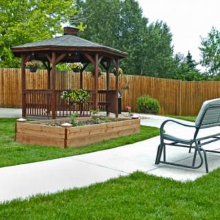 A peaceful backyard featuring a wooden gazebo surrounded by greenery and a paved pathway.
