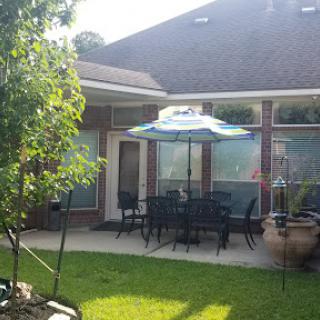 A cozy outdoor patio with seating under an umbrella, surrounded by greenery.